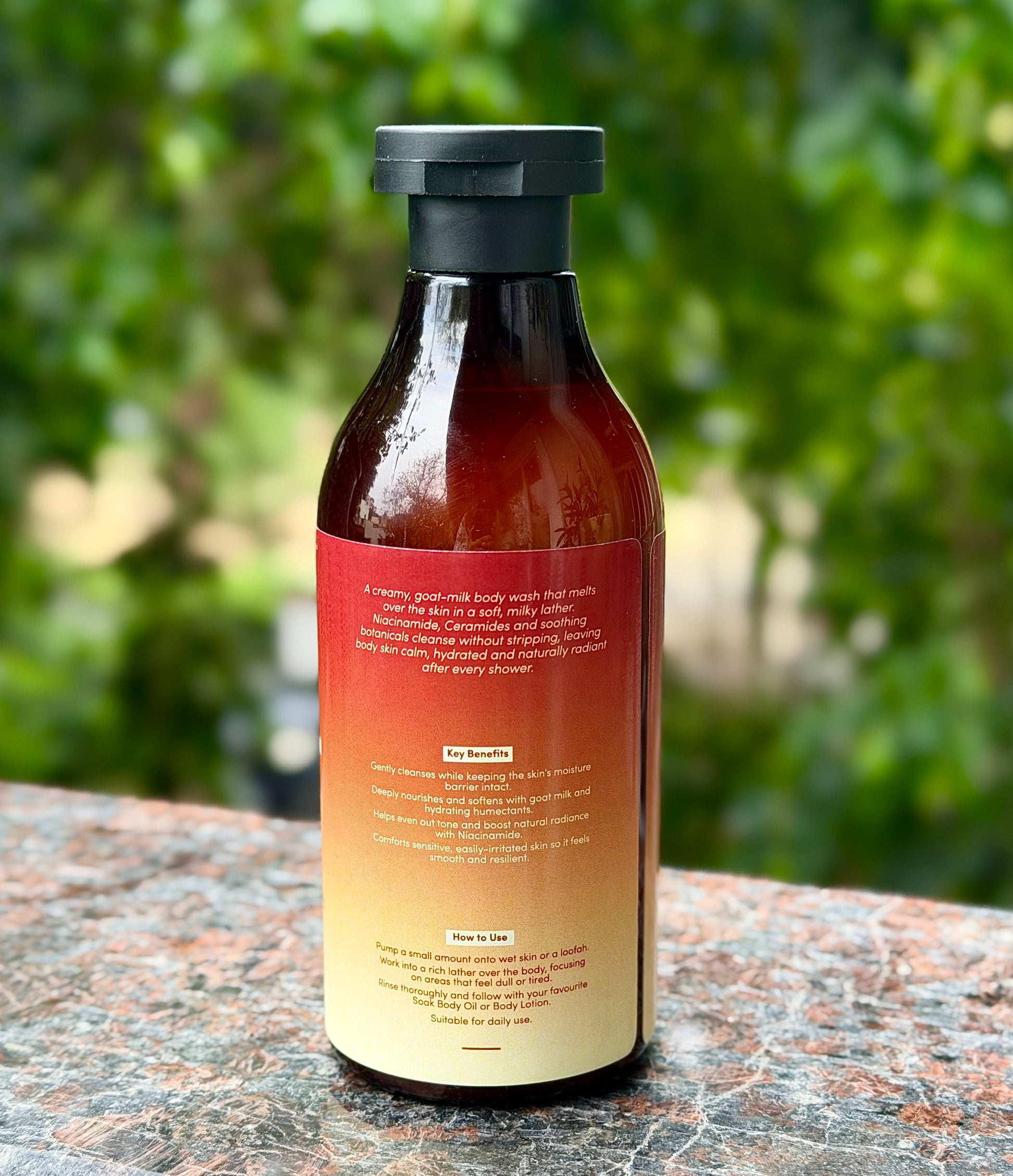 Bottle of Soak Studio body wash with a red label on a stone surface with greenery in the background